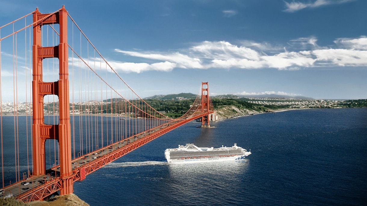 A Princess cruise ship passing under the Golden Gate Bridge in San Francisco, with the city skyline and rolling hills in the background.