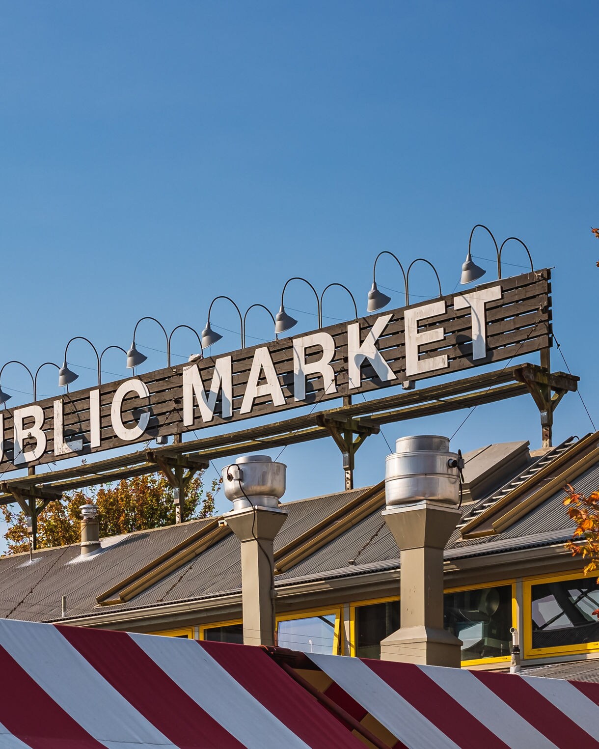 Granville Island Public Market sign above striped red-and-white awnings under a clear blue sky.