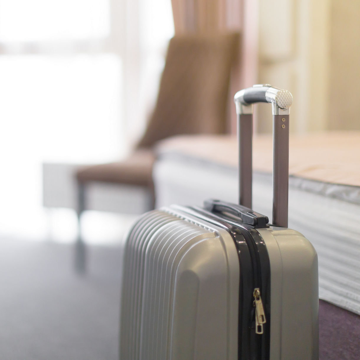 Silver suitcase in bright hotel room interior.