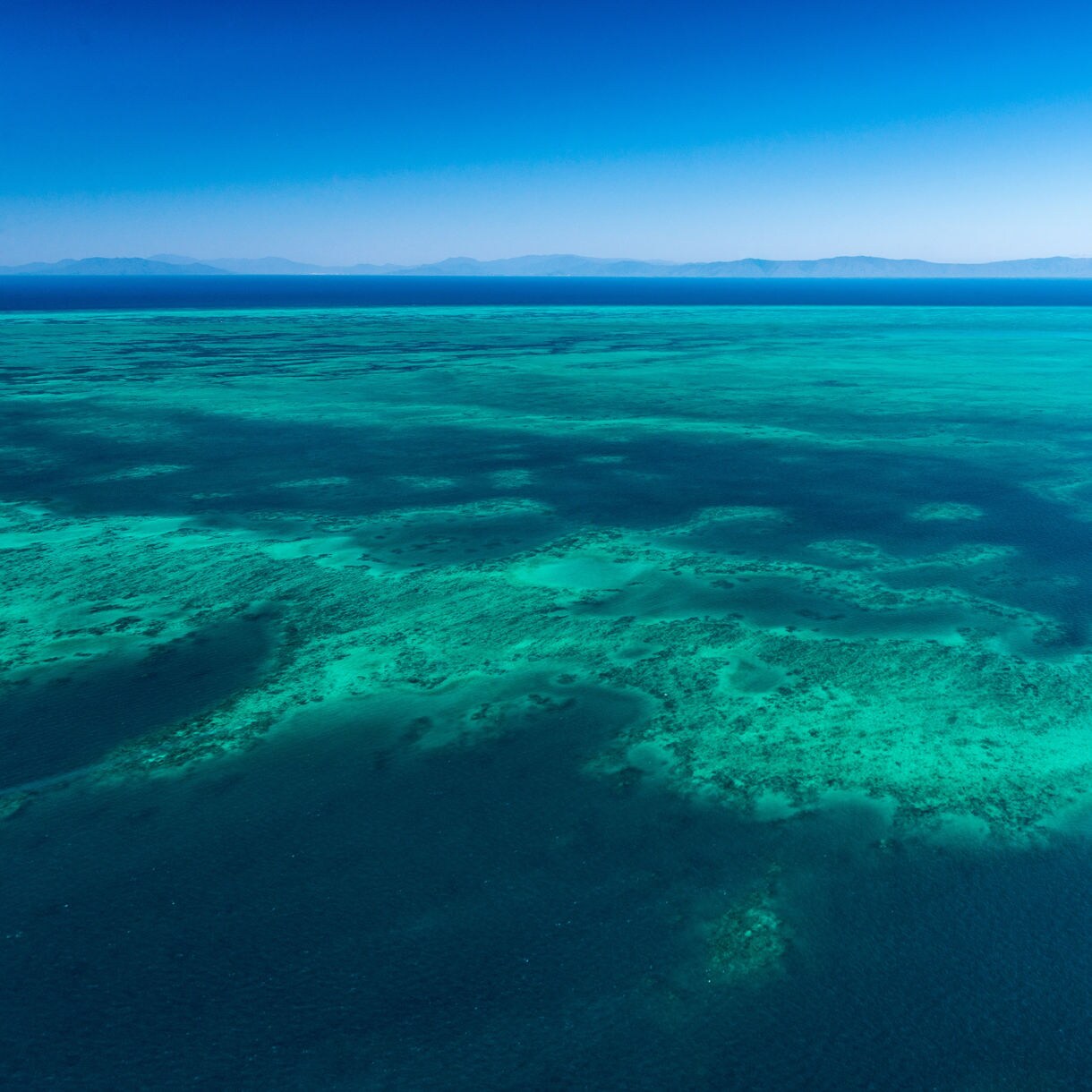 Aerial view of the Great Barrier Reef’s shallow turquoise waters fading into deep blue.