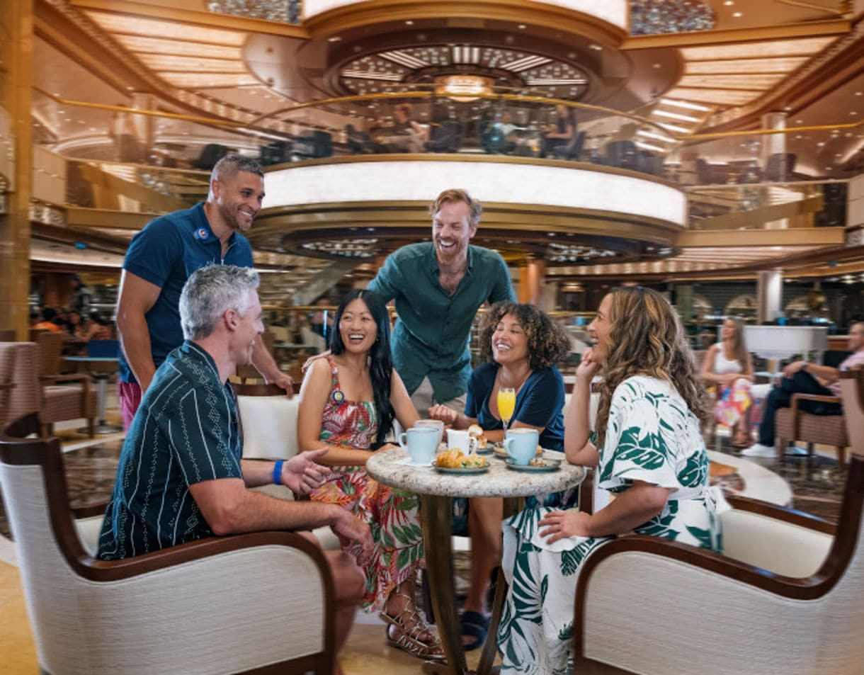 Group of people laughing and socializing around café table in elegant setting.