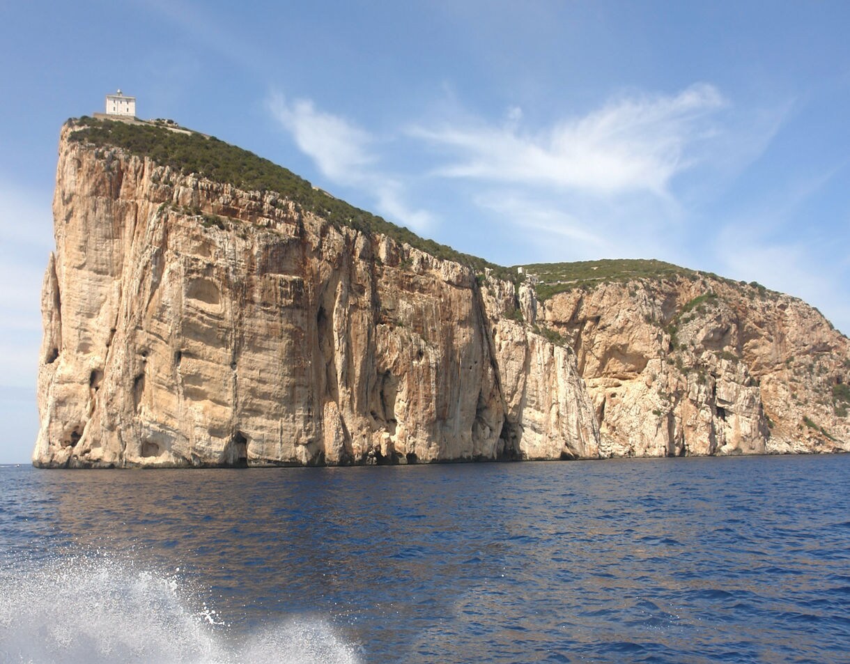 Tall rugged limestone cliffs overlooking deep blue water under a bright sky.