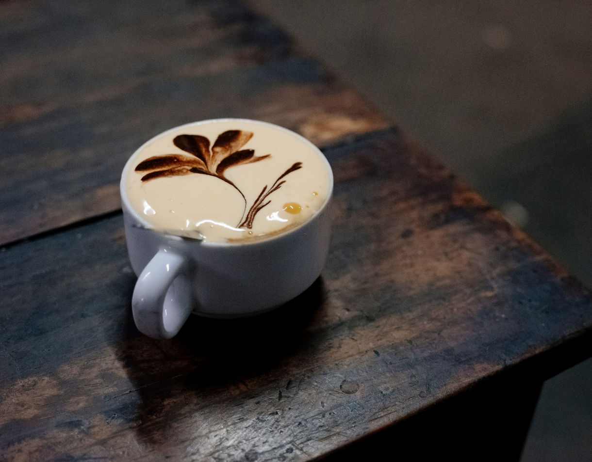 White cup of Vietnamese egg coffee with thick frothy cream and cocoa leaf design, set on a rustic wooden table.