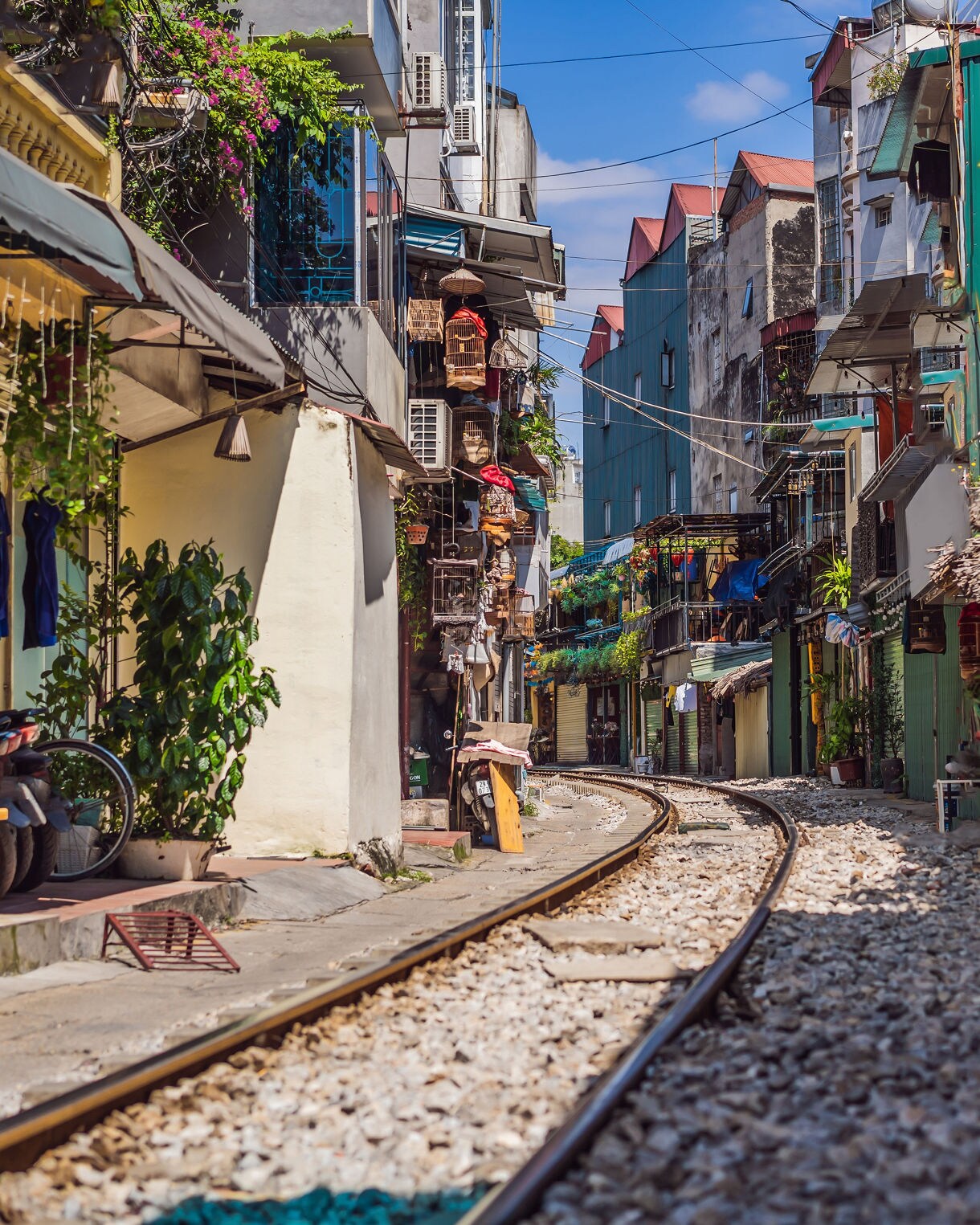 Railway line running through Hanoi’s Train Street, flanked by tall, narrow houses, hanging plants and small cafes with locals sitting nearby.