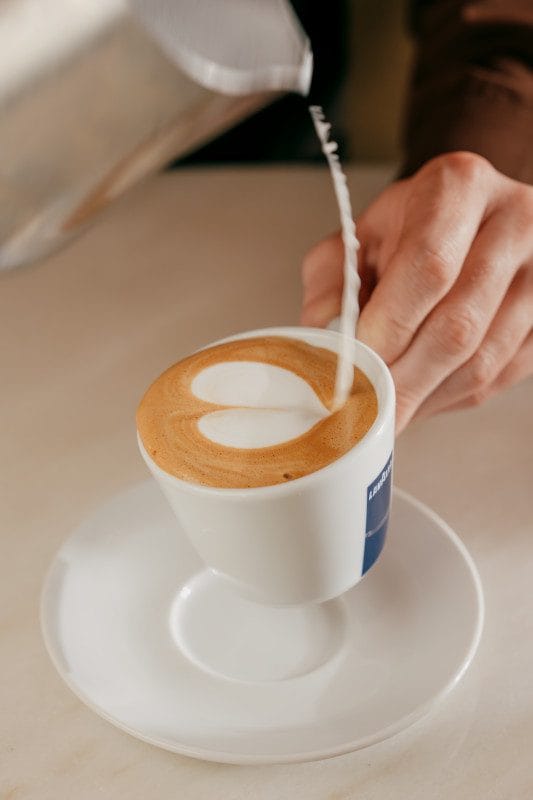 Hand pouring steamed milk into coffee to create heart latte art.