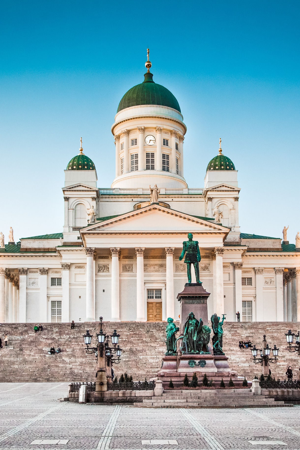 A view of Helsinki Cathedral in Finland, featuring its iconic green domes and neoclassical architecture, with the statue of Emperor Alexander II in the foreground at Senate Square.