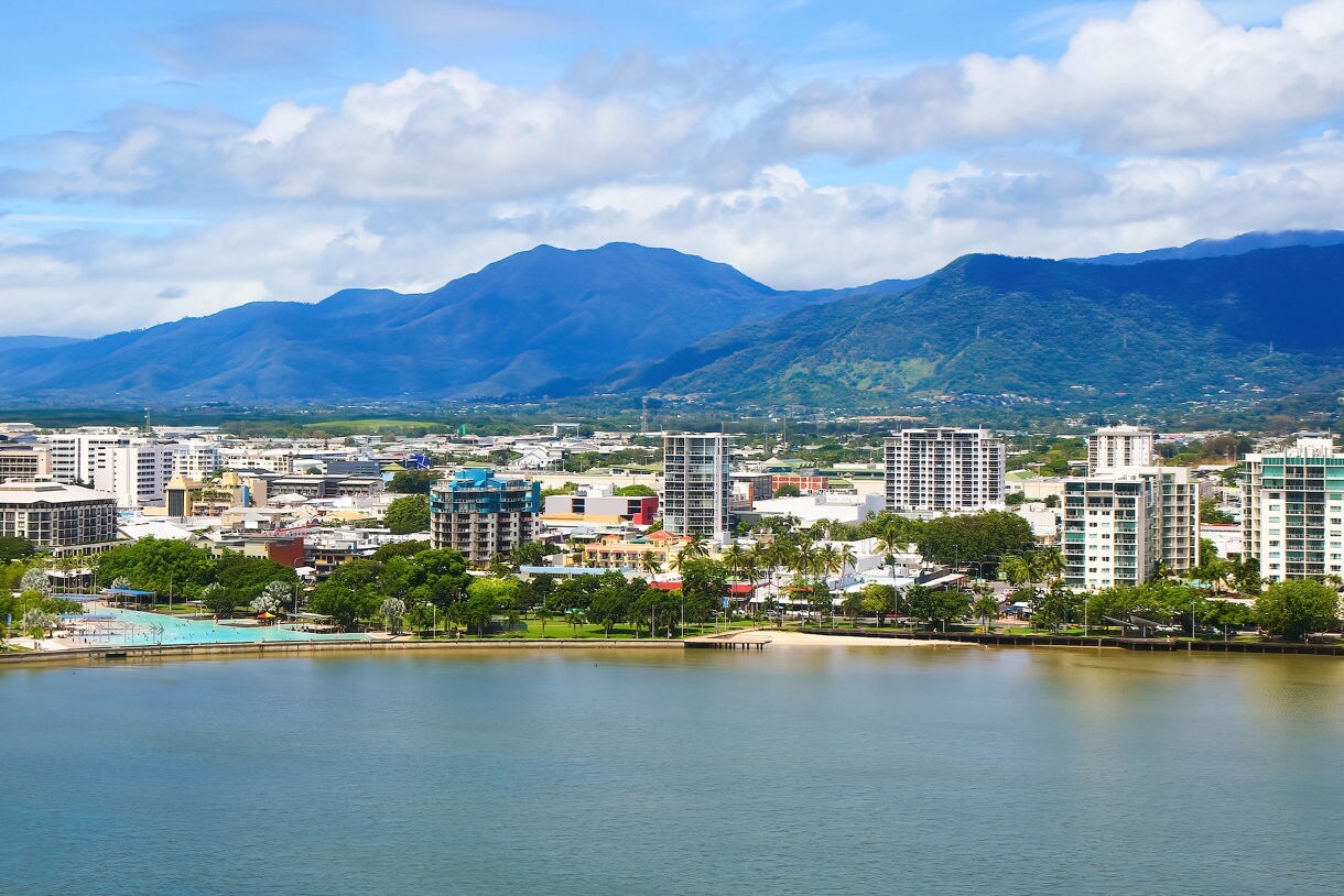 Colorful boats docked at a marina in Cairns with lush green hills and a bright blue sky in the background.
