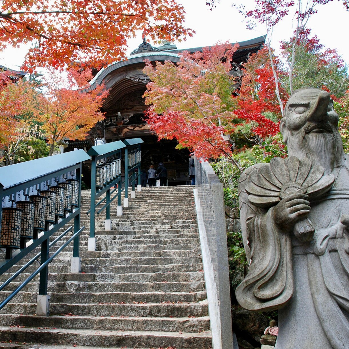 Stone staircase leading to Daishoin Temple on Miyajima Island, flanked by vibrant red and orange maple trees.