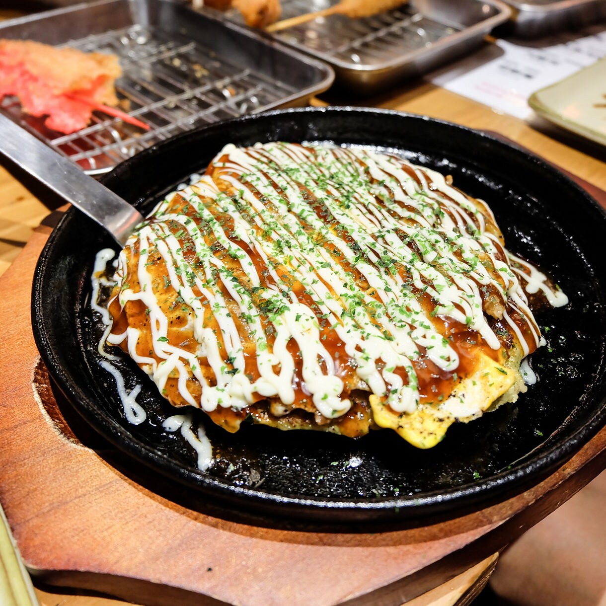 Close-up of Hiroshima-style okonomiyaki topped with drizzled sauces, mayonnaise, seaweed and savory ingredients.