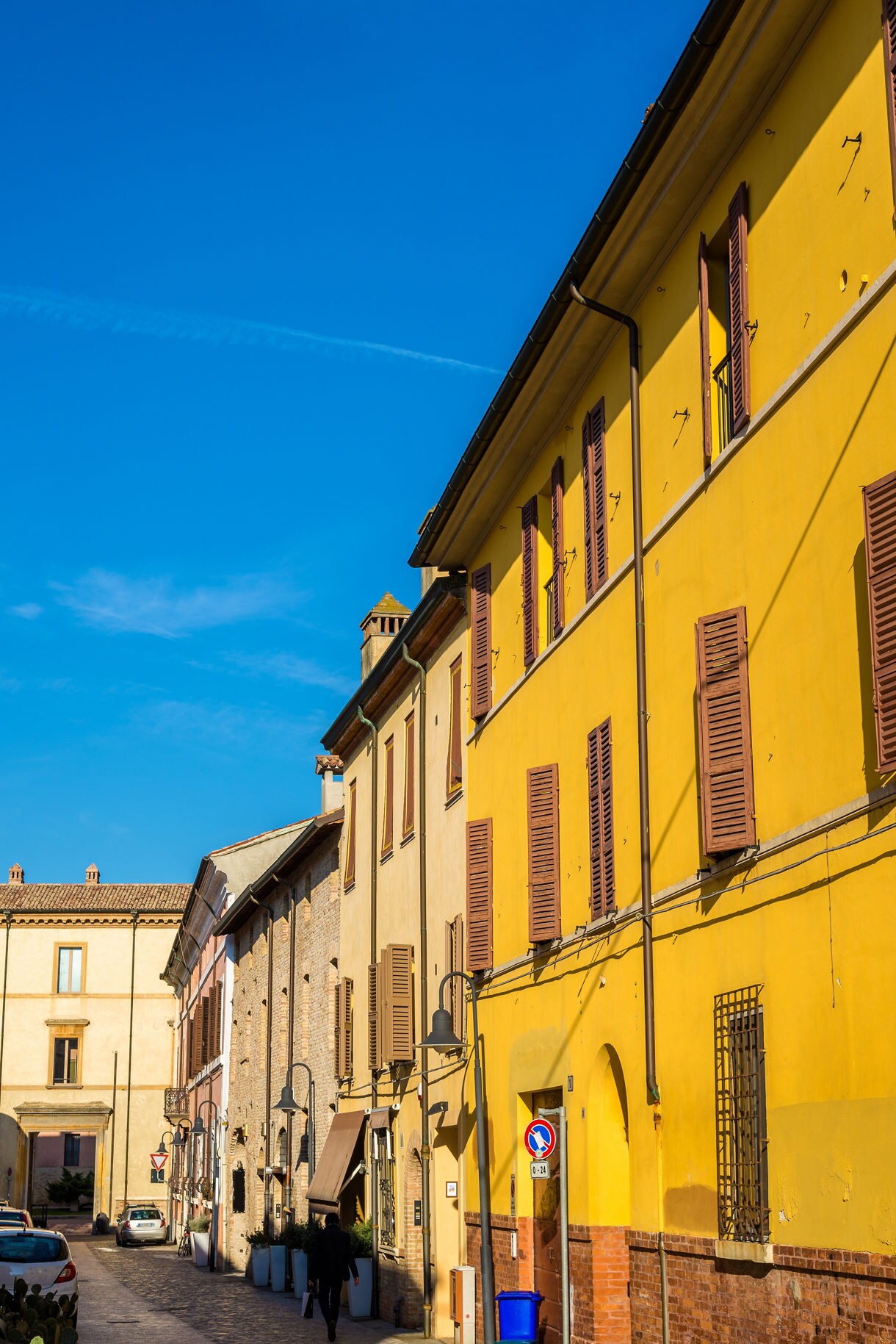 Colorful historic street in Ravenna lined with yellow and brick buildings beneath a clear blue sky.