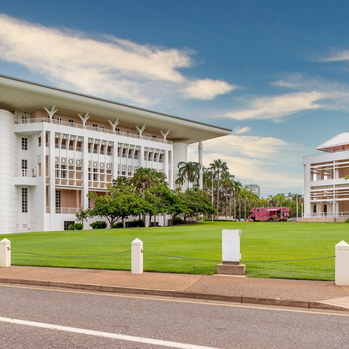 White Parliament House building in Darwin surrounded by palm trees and manicured lawns under a bright tropical sky.