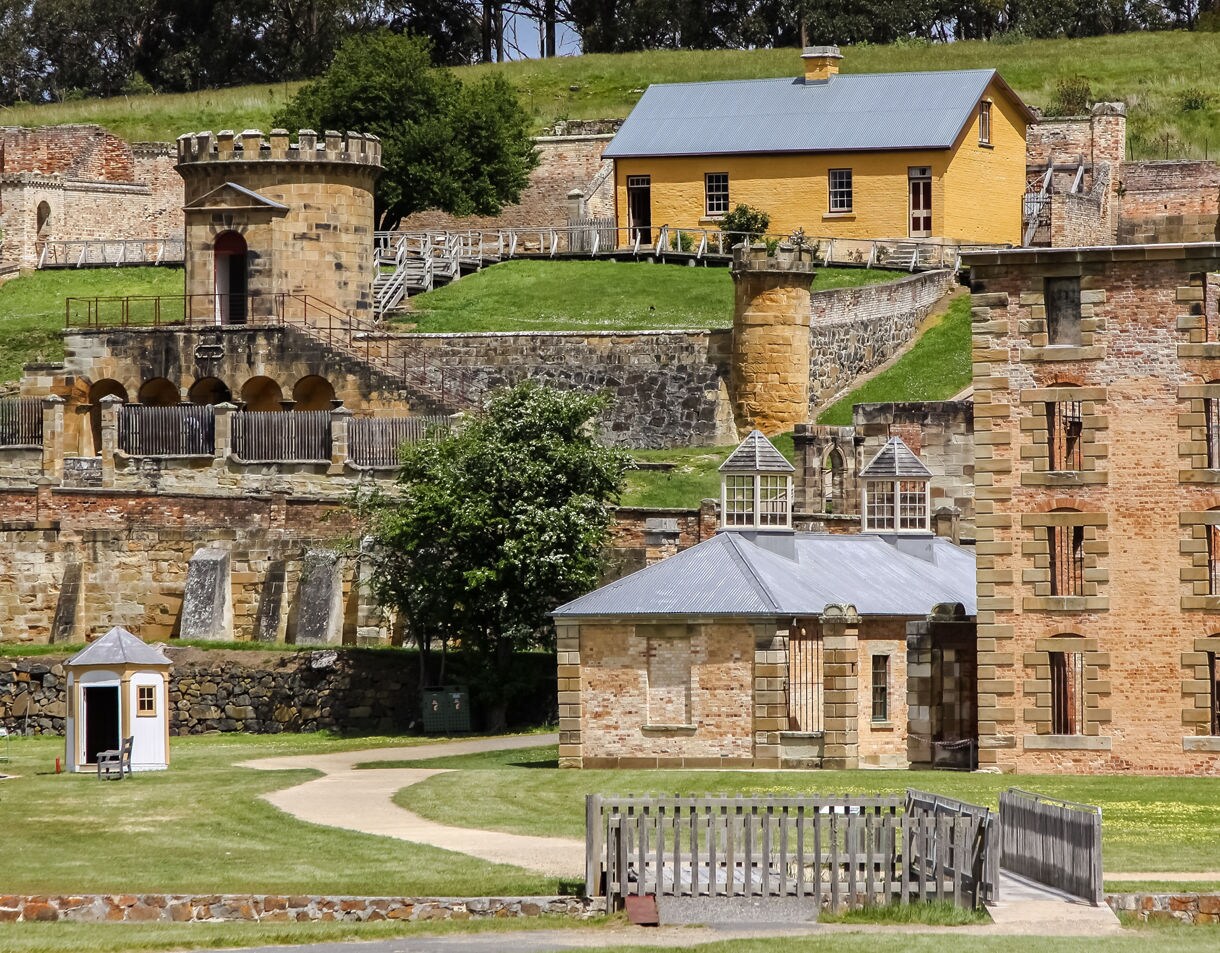 Close view of historic sandstone and brick buildings at Port Arthur in Tasmania featuring barred windows, stone terraces and grassy pathways on a sunny day.