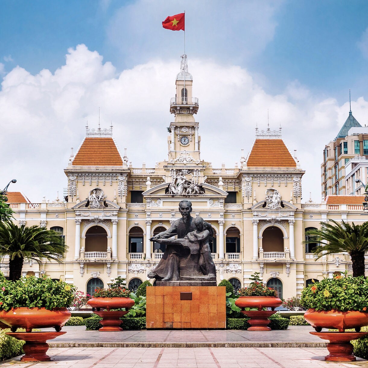 Ho Chi Minh City Hall in Vietnam with its ornate French colonial architecture, orange roof tiles and statue of Ho Chi Minh surrounded by manicured greenery.