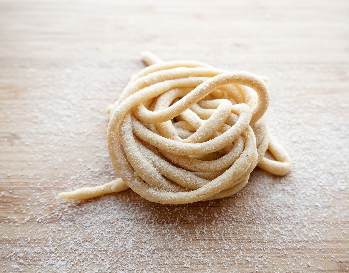 A small coil of uncooked handmade pasta dusted with flour on a wooden surface.