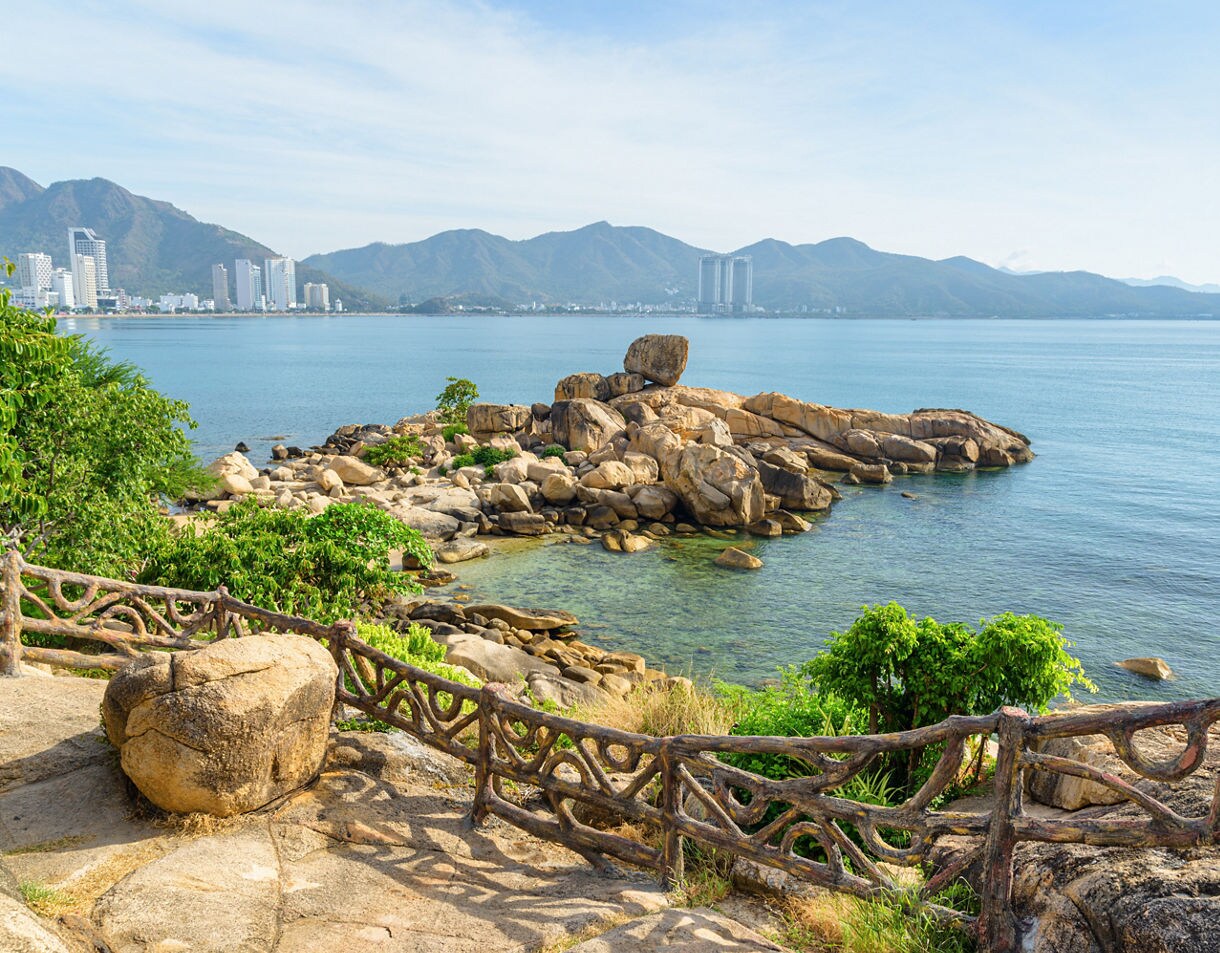 Rocky outcrop at Hon Chong Promontory in Nha Trang, Vietnam, overlooking clear turquoise waters and a distant skyline backed by mountains.