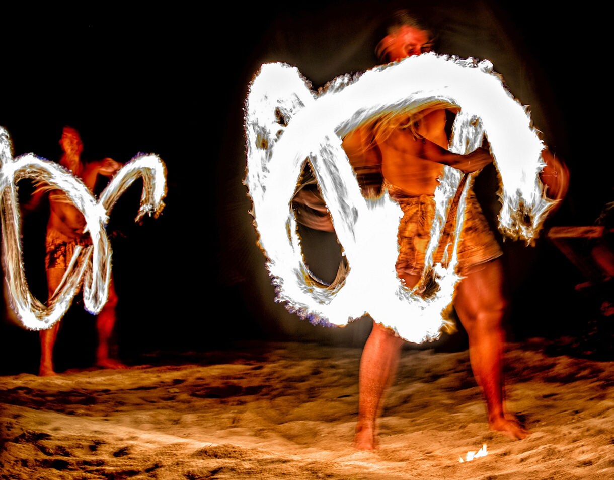 Fire dancer performing at night, spinning blazing torches that leave glowing trails in the air.