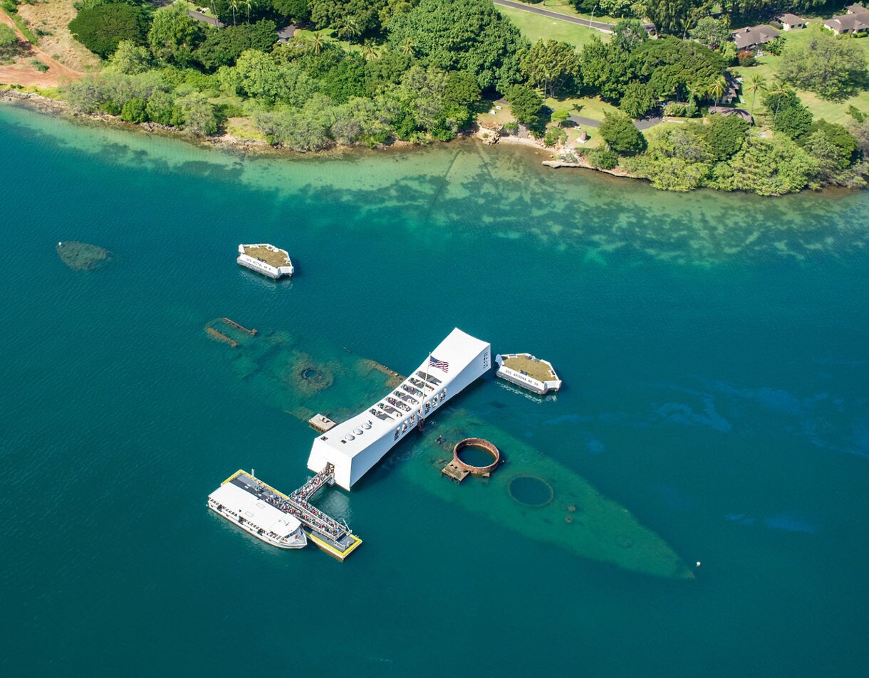 Aerial view of the USS Arizona Memorial spanning the sunken battleship in the blue waters of Pearl Harbor.