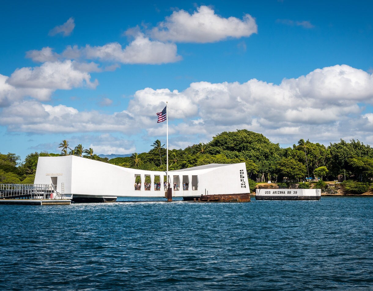 White USS Arizona Memorial structure with American flag, sitting on the water at Pearl Harbor in Honolulu.