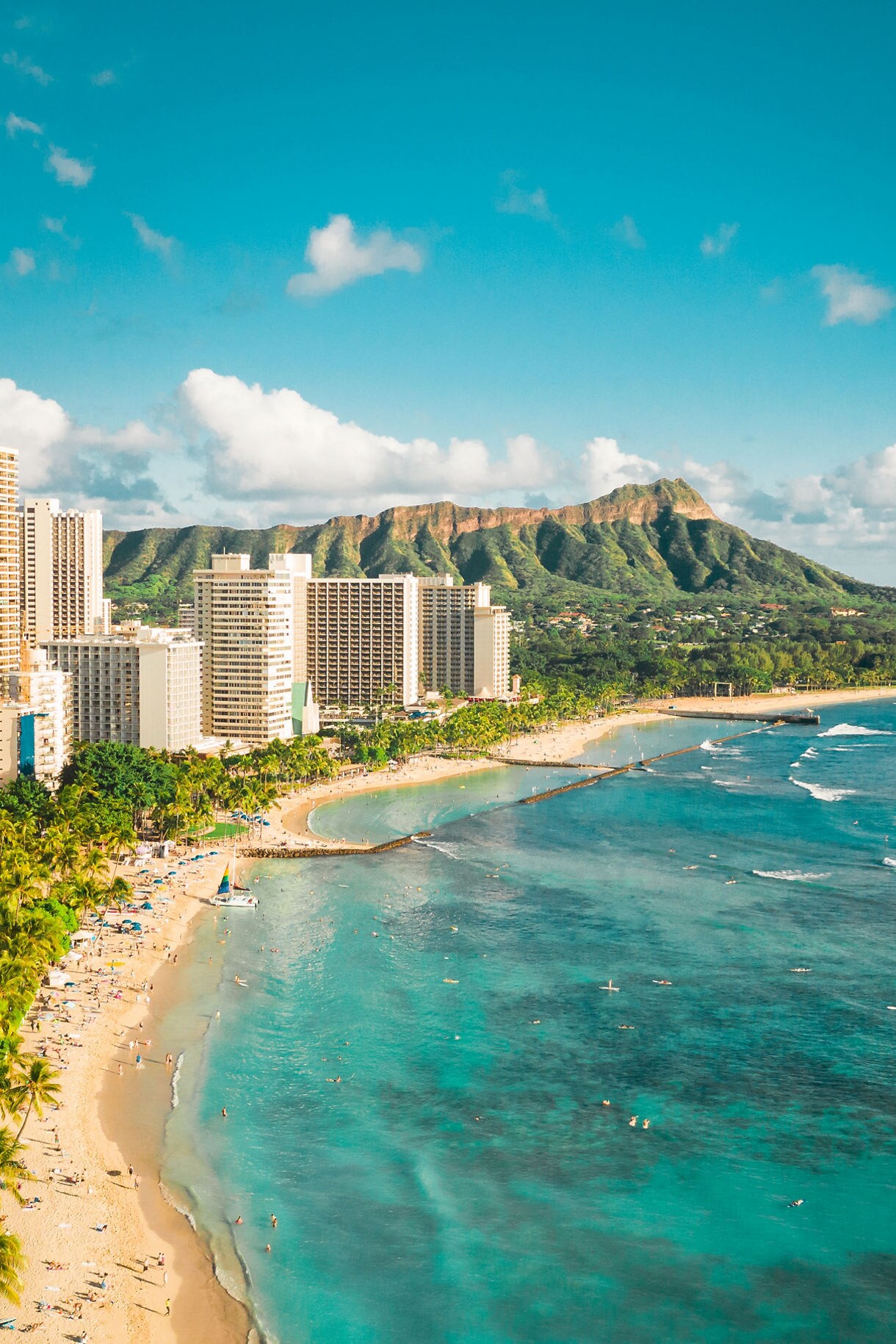Aerial view of Waikiki Beach with turquoise waters, high-rise hotels, and Diamond Head crater in the background.