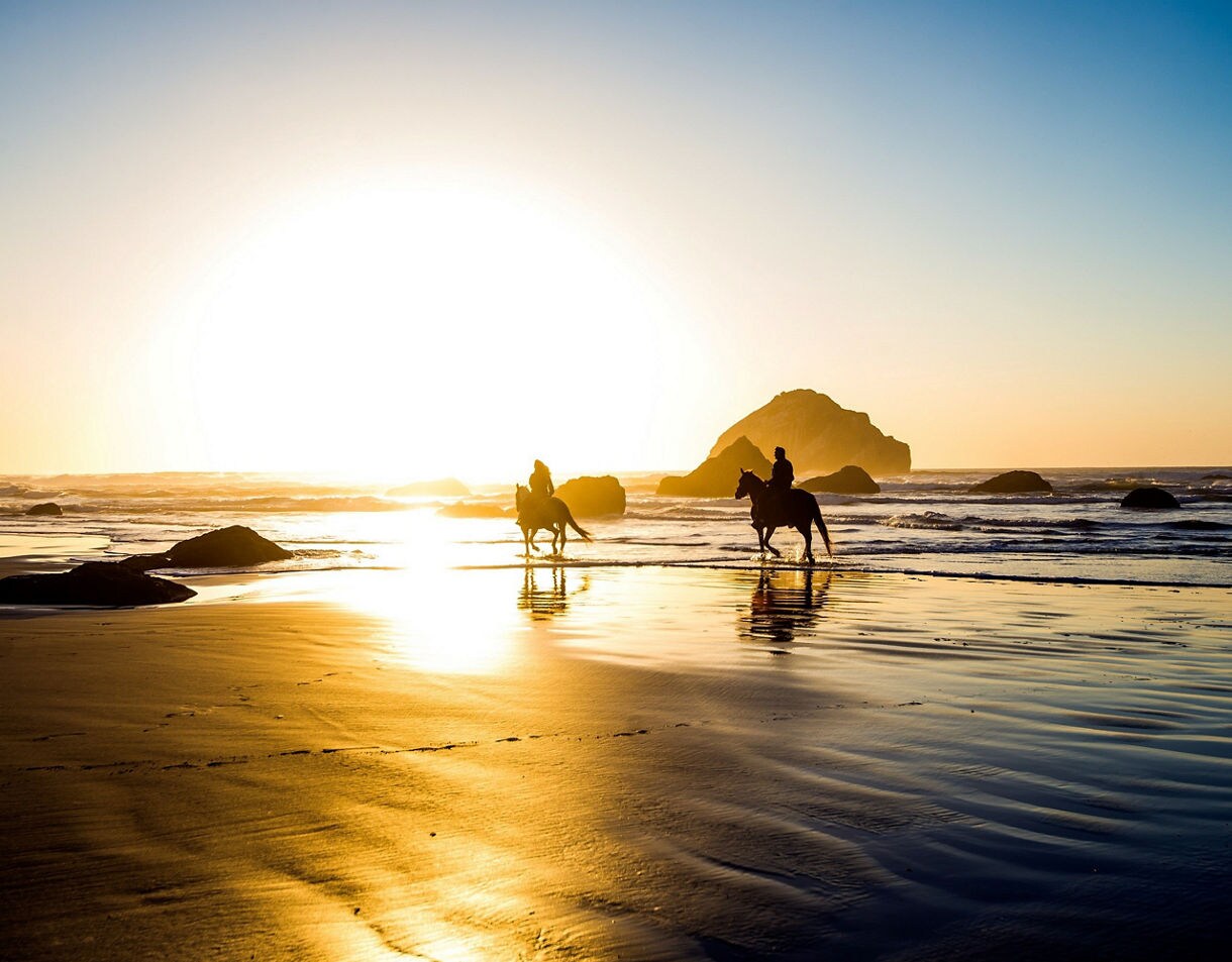 A group of people riding horses on the sandy beach of St. Maarten at sunset.