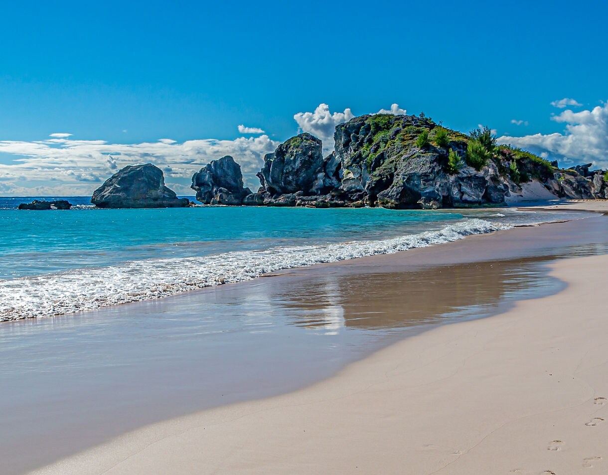 Horseshoe Bay Beach in Bermuda with soft pink sand, turquoise water and rugged rock formations under a bright blue sky.