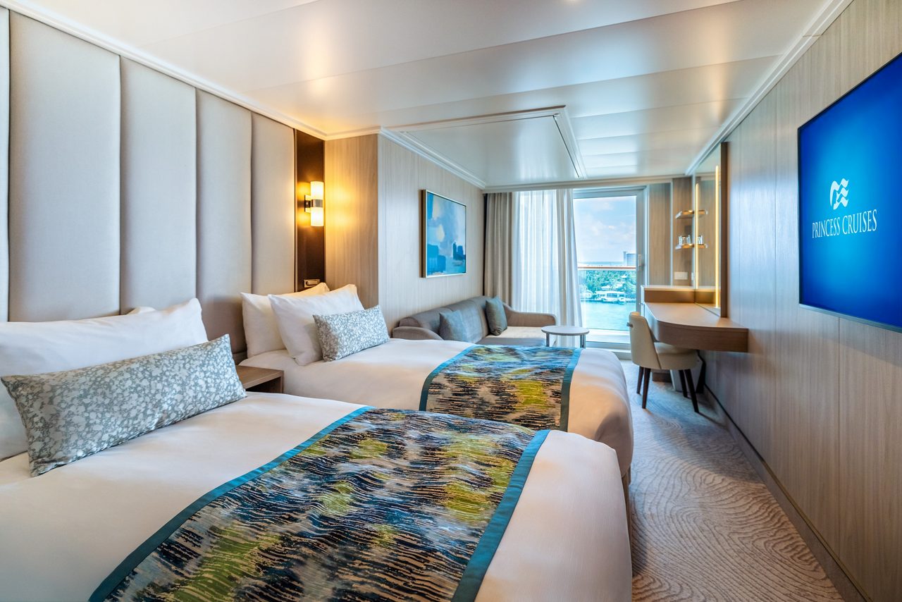 A bright, modern Princess Cruises accessible stateroom with two beds, a large window, and a wall-mounted TV displaying the Princess Cruises logo.