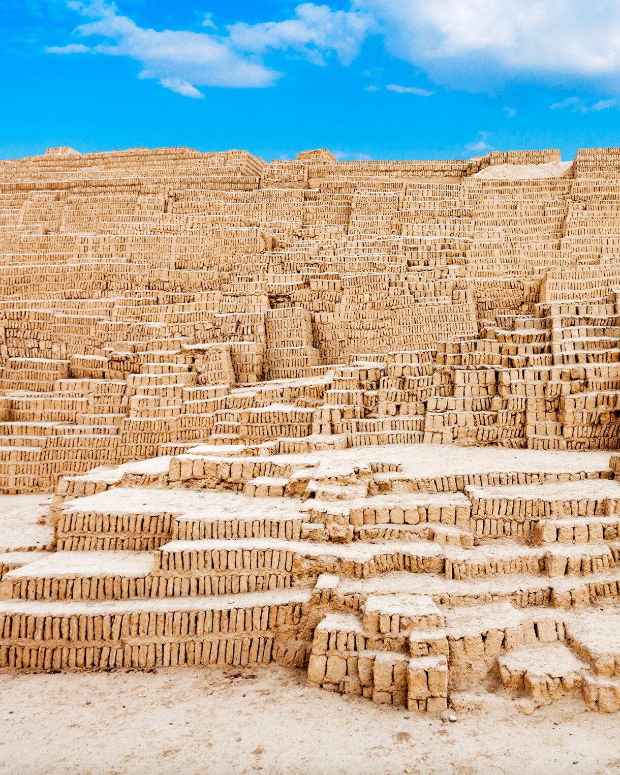 Adobe brick terraces of the ancient Huaca Pucllana pyramid in Lima, showing layered mud-brick construction under a bright blue sky.