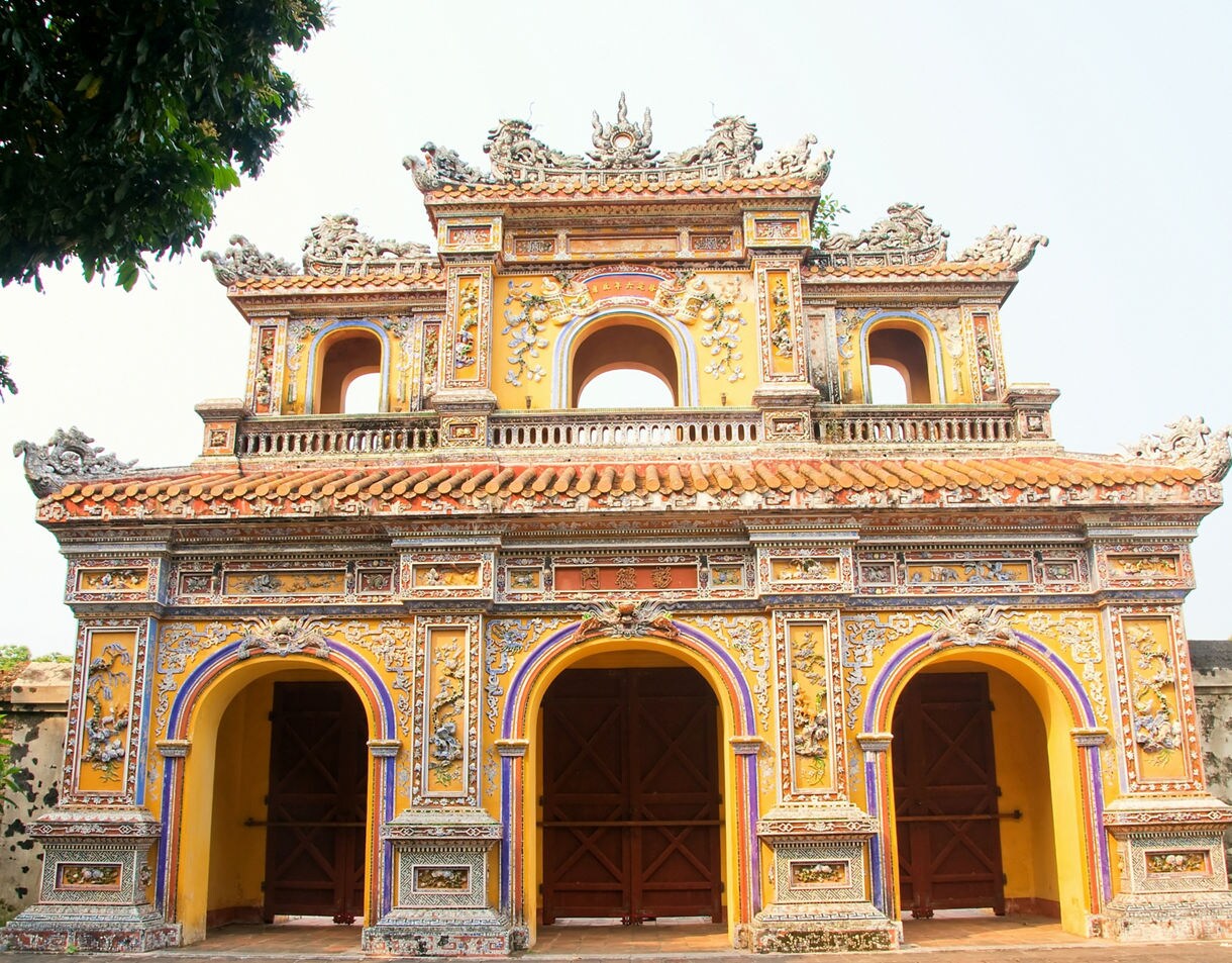 The colorful Ngo Mon Gate at the Imperial City in Hue, Vietnam, featuring intricate carvings, arched doorways and dragon motifs on a bright yellow facade.