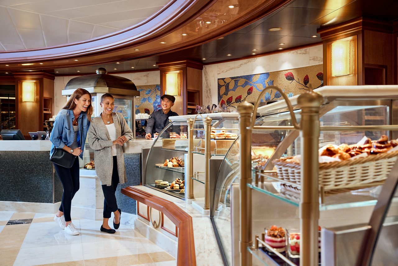 People browsing pastry display case with assorted desserts and baked goods.