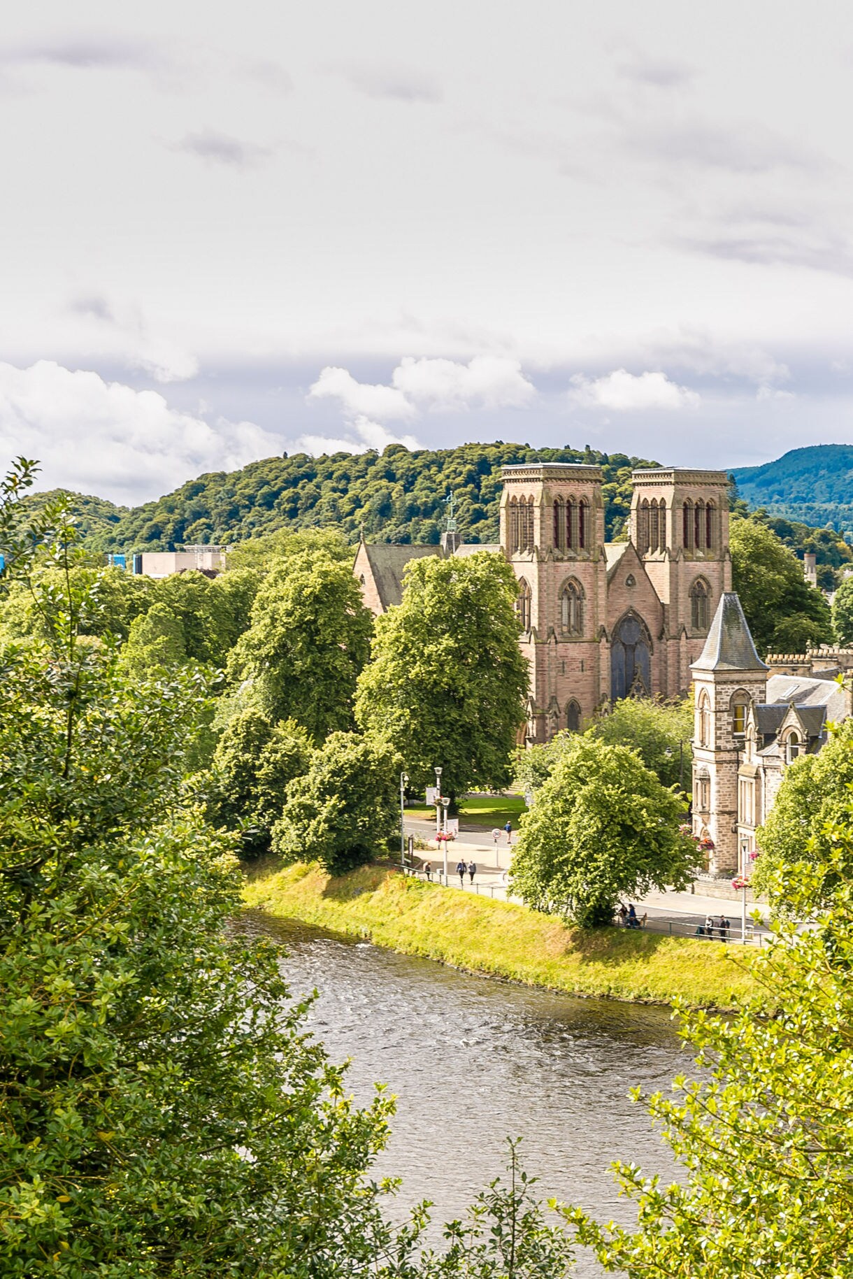 Inverness view with St Andrew’s Cathedral rising above trees along the River Ness on a partly cloudy day.