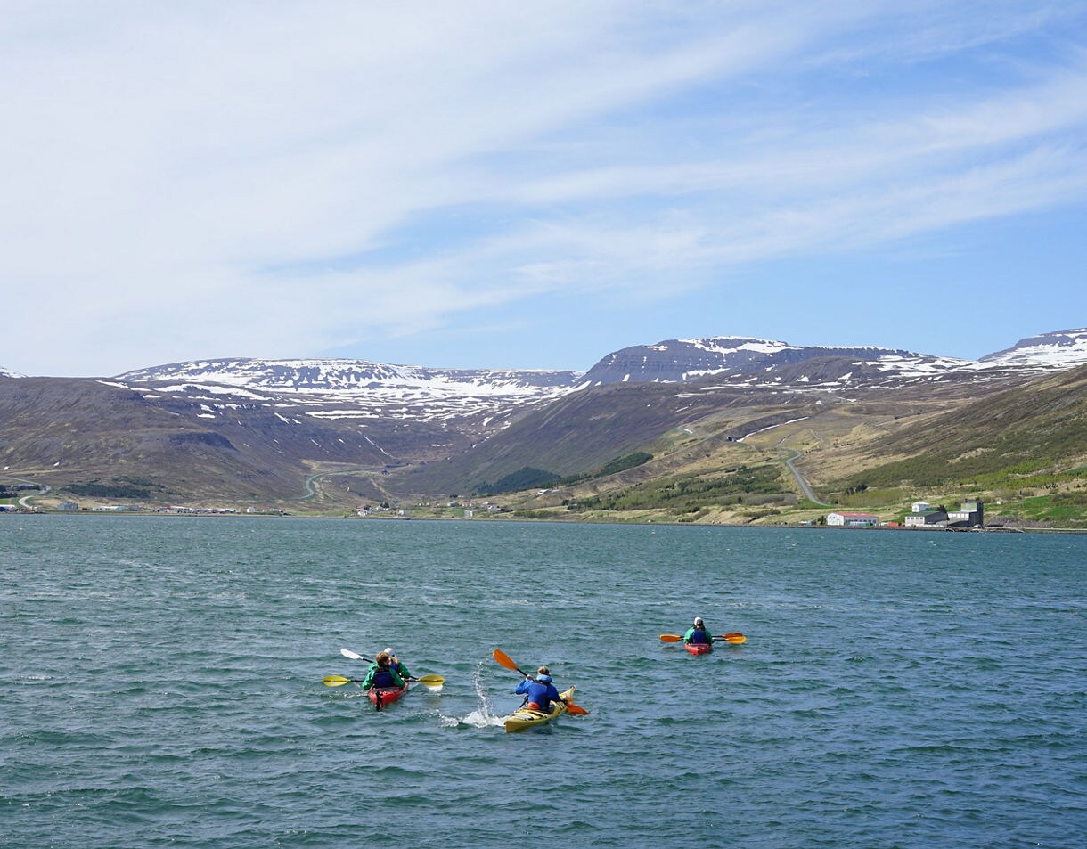 Three kayakers on Ísafjörður fjord with snow-capped mountains in the background.