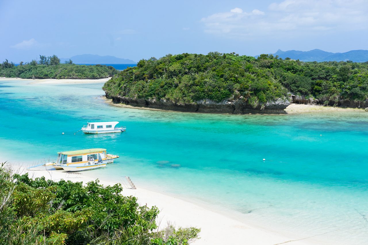 Clear turquoise water, white sand and tour boats at Kabira Bay with lush islets nearby.