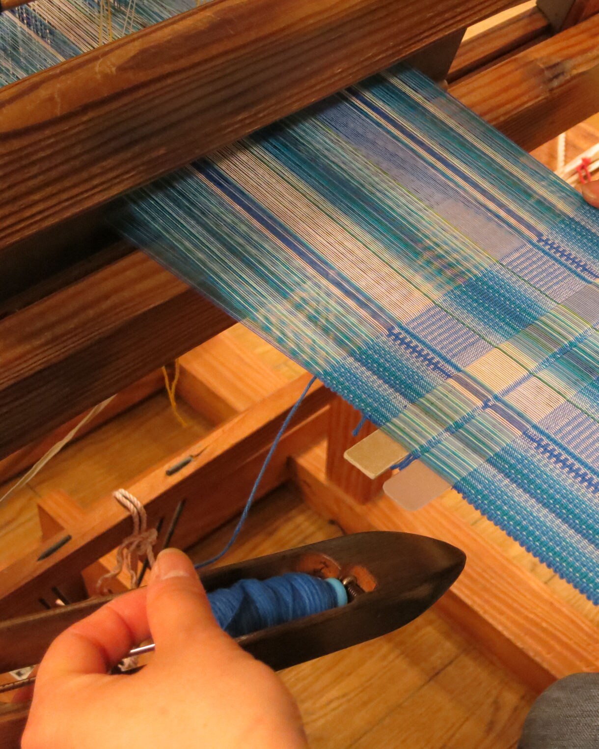 Close-up of hands weaving blue patterned fabric on a wooden loom.