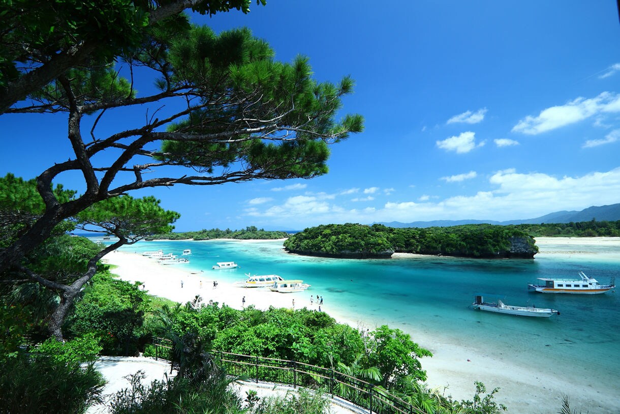 Boats float on clear blue water near white sand and green islets at Kabira Bay.