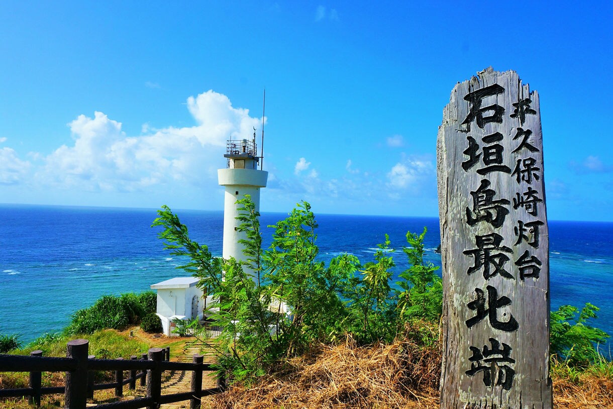 White lighthouse and ocean view behind a wooden sign at Cape Hirakubo on Ishigaki.
