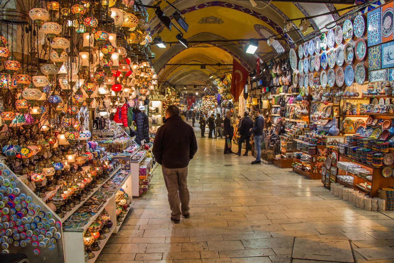 Interior of Istanbul’s Grand Bazaar with hanging mosaic lamps, shelves of ceramics, and shoppers browsing vibrant stalls.