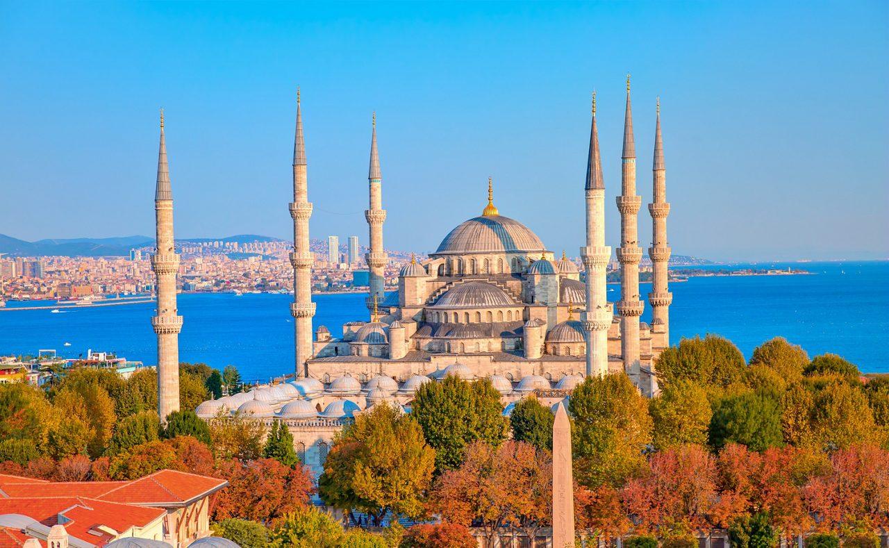 The Blue Mosque in Istanbul with six slender minarets and cascading domes, set against the deep blue waters of the Sea of Marmara.