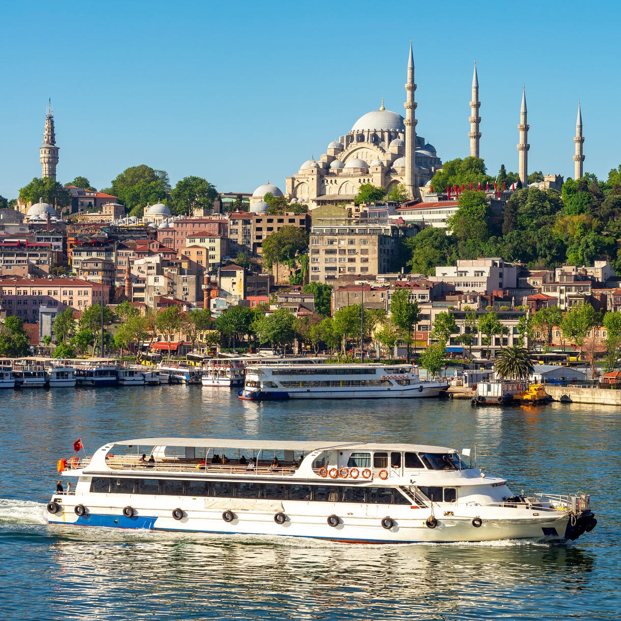 A passenger boat cruising the Bosphorus with the Suleymaniye Mosque and hillside cityscape in the background.