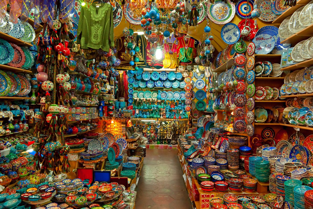A vibrant stall in the Grand Bazaar filled with shelves of colorful ceramic plates, bowls, and hanging ornaments.