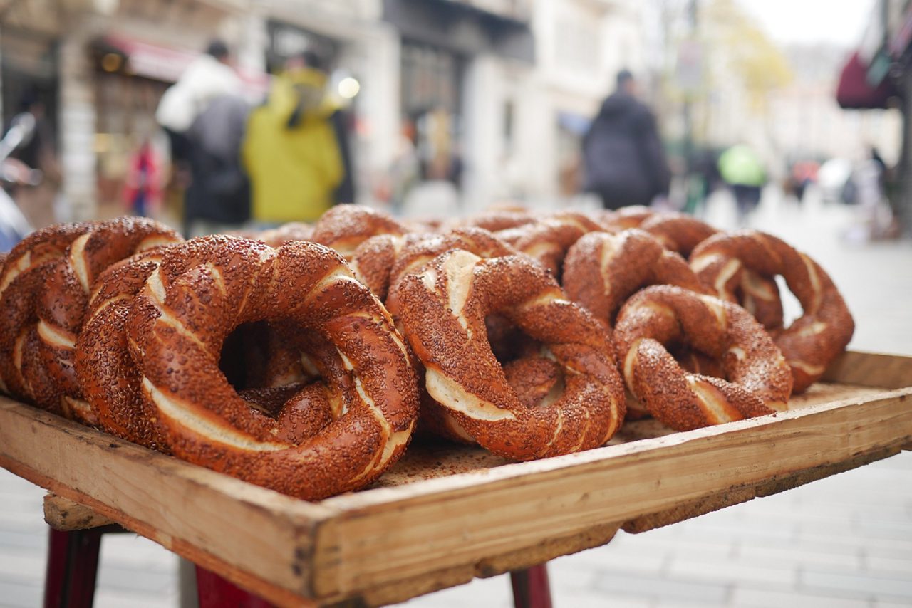 A tray of golden brown Turkish simit bread rings covered in sesame seeds displayed at a street market.