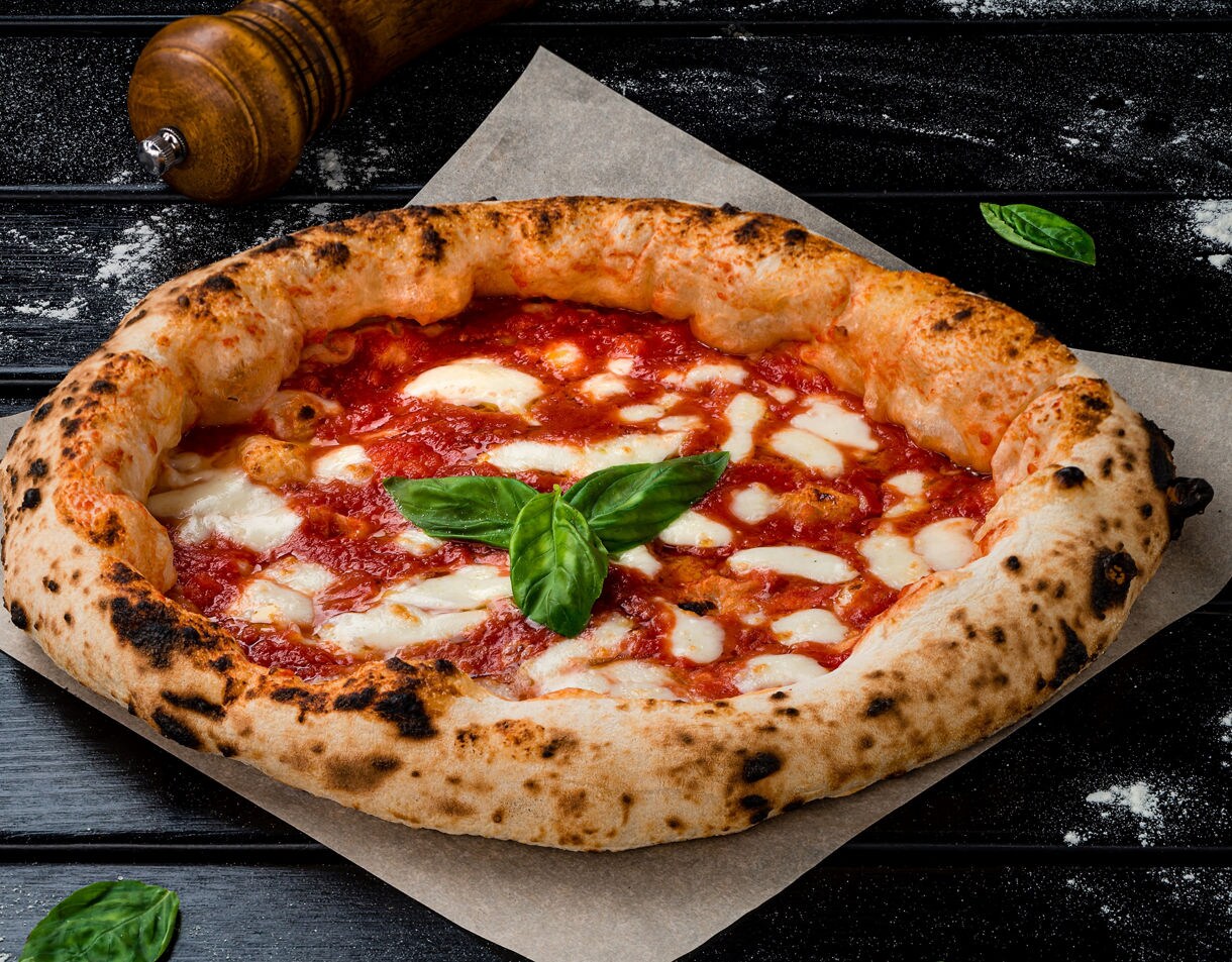 A Margherita pizza with a puffy charred crust, melted mozzarella, bright tomato sauce and a basil garnish on parchment paper.