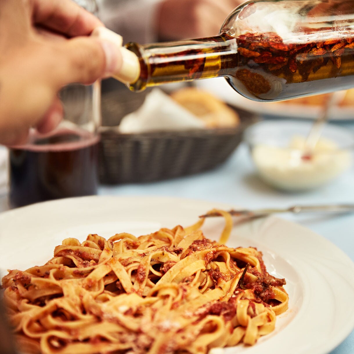 A plate of pasta being drizzled with olive oil, showcasing authentic Italian flavors.