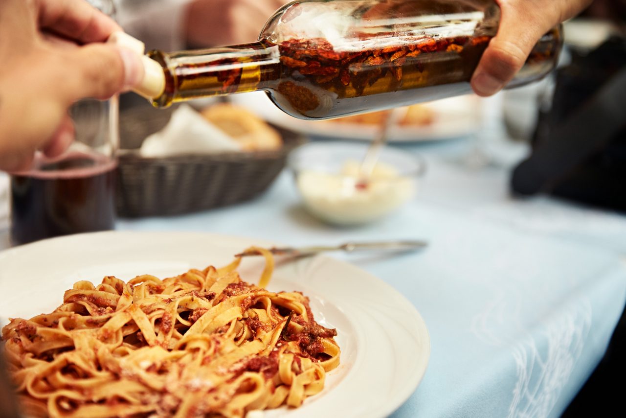 A plate of pasta being drizzled with olive oil, showcasing authentic Italian flavors.
