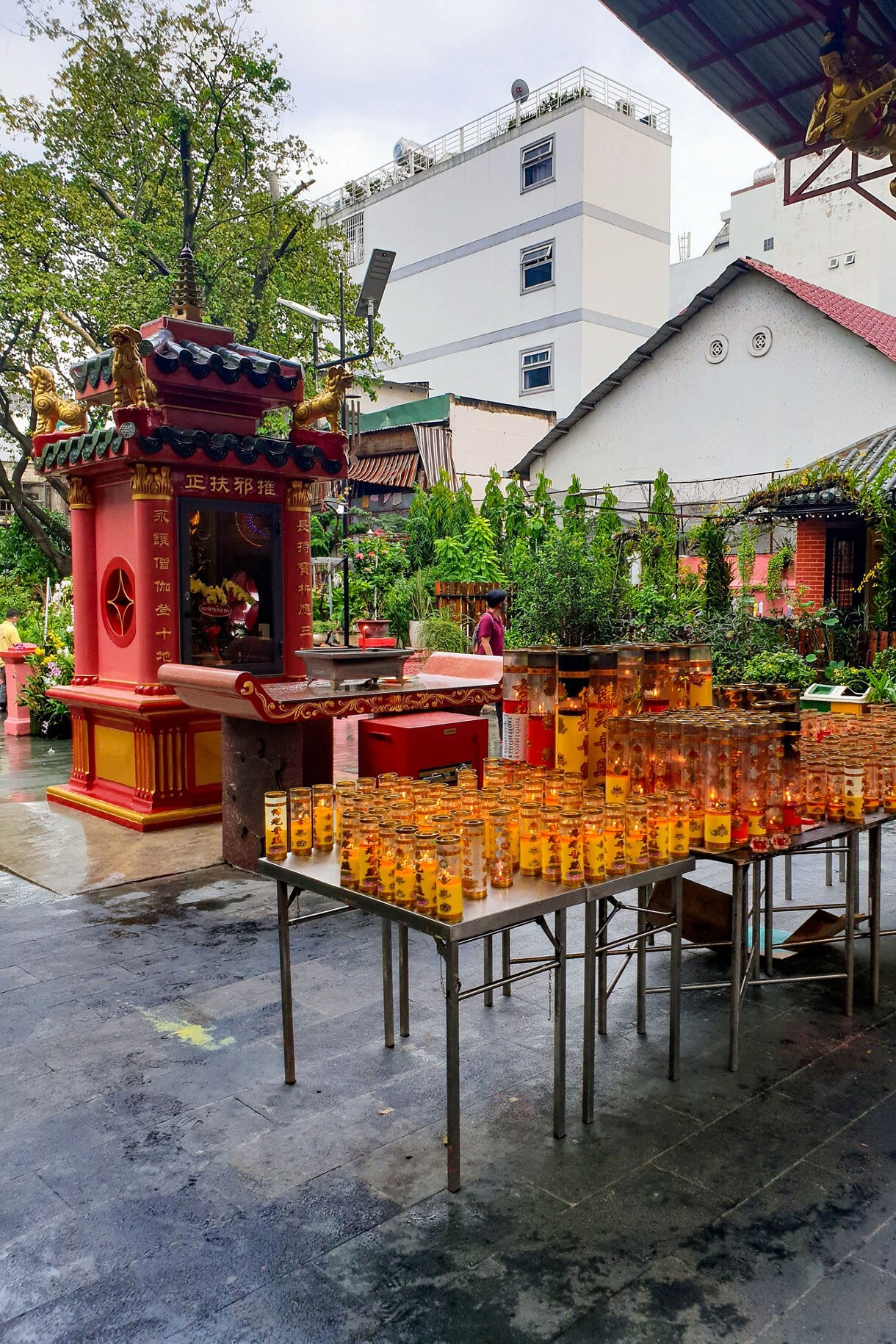 Rows of glowing candles arranged on tables in the courtyard of the Jade Emperor Pagoda, surrounded by red shrines and greenery.