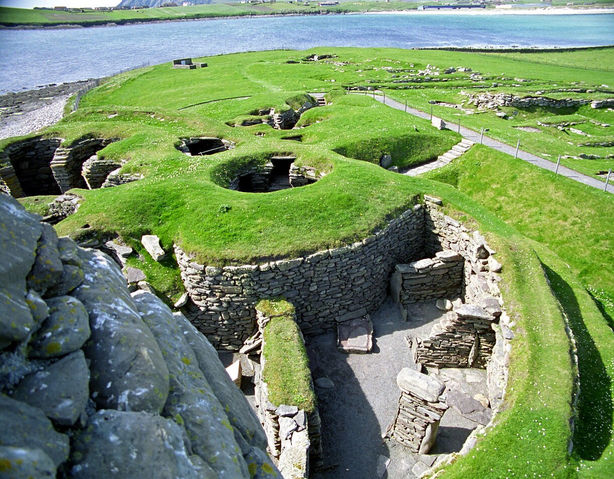 Archaeological site of Jarlshof in Shetland, featuring stone ruins of prehistoric houses covered in grass near the sea.