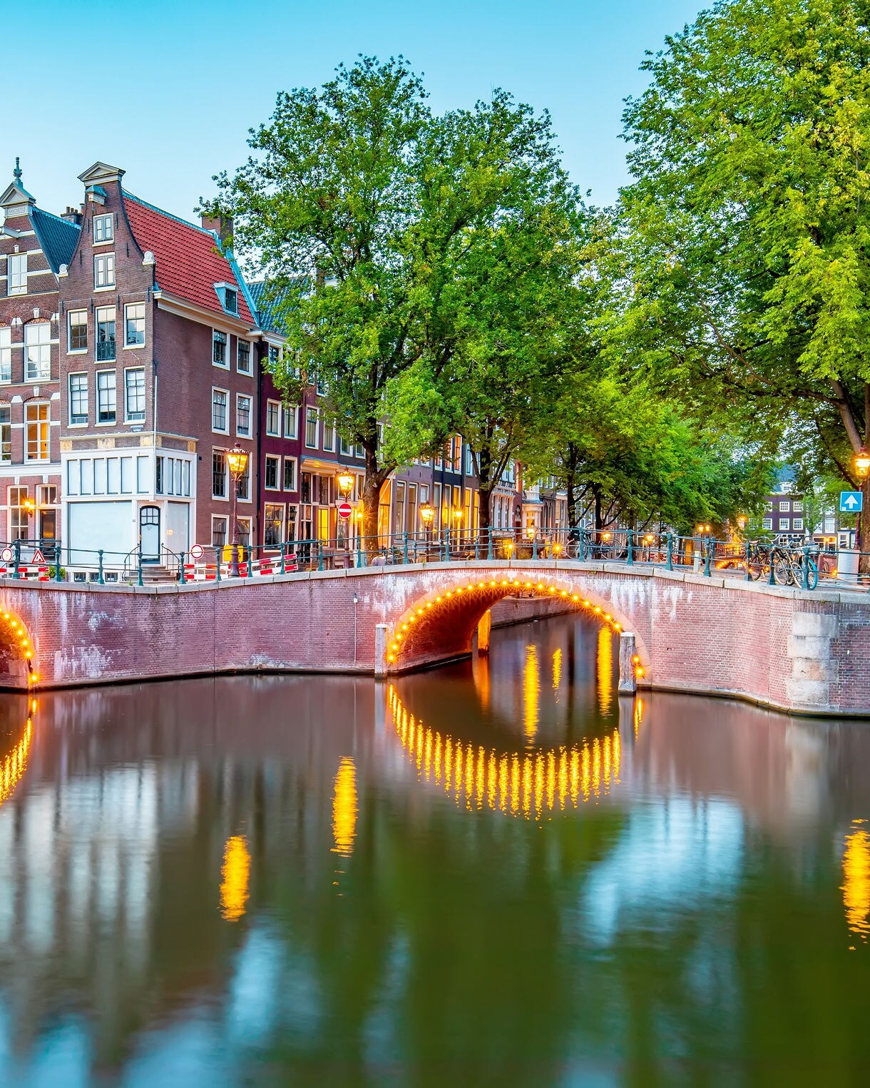 Evening view of illuminated canal bridges and historic houses in Amsterdam’s Jordaan district.