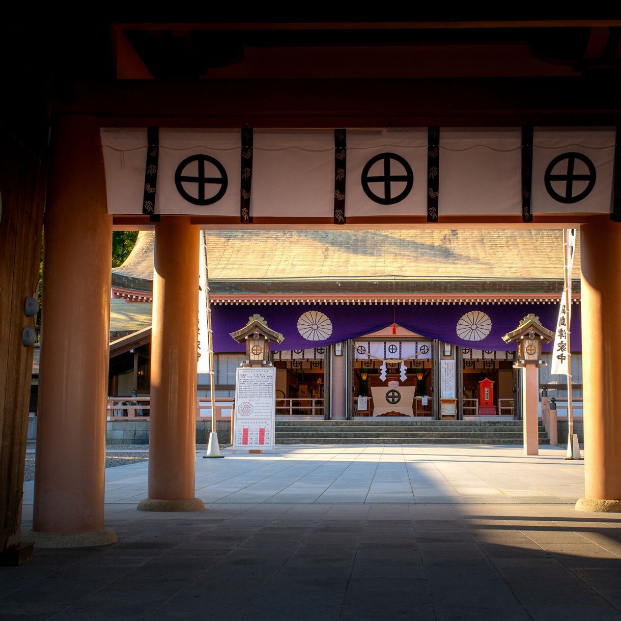 View through a wooden gate of Terukuni Shrine in Kagoshima, showing the main hall adorned with purple banners and traditional emblems.