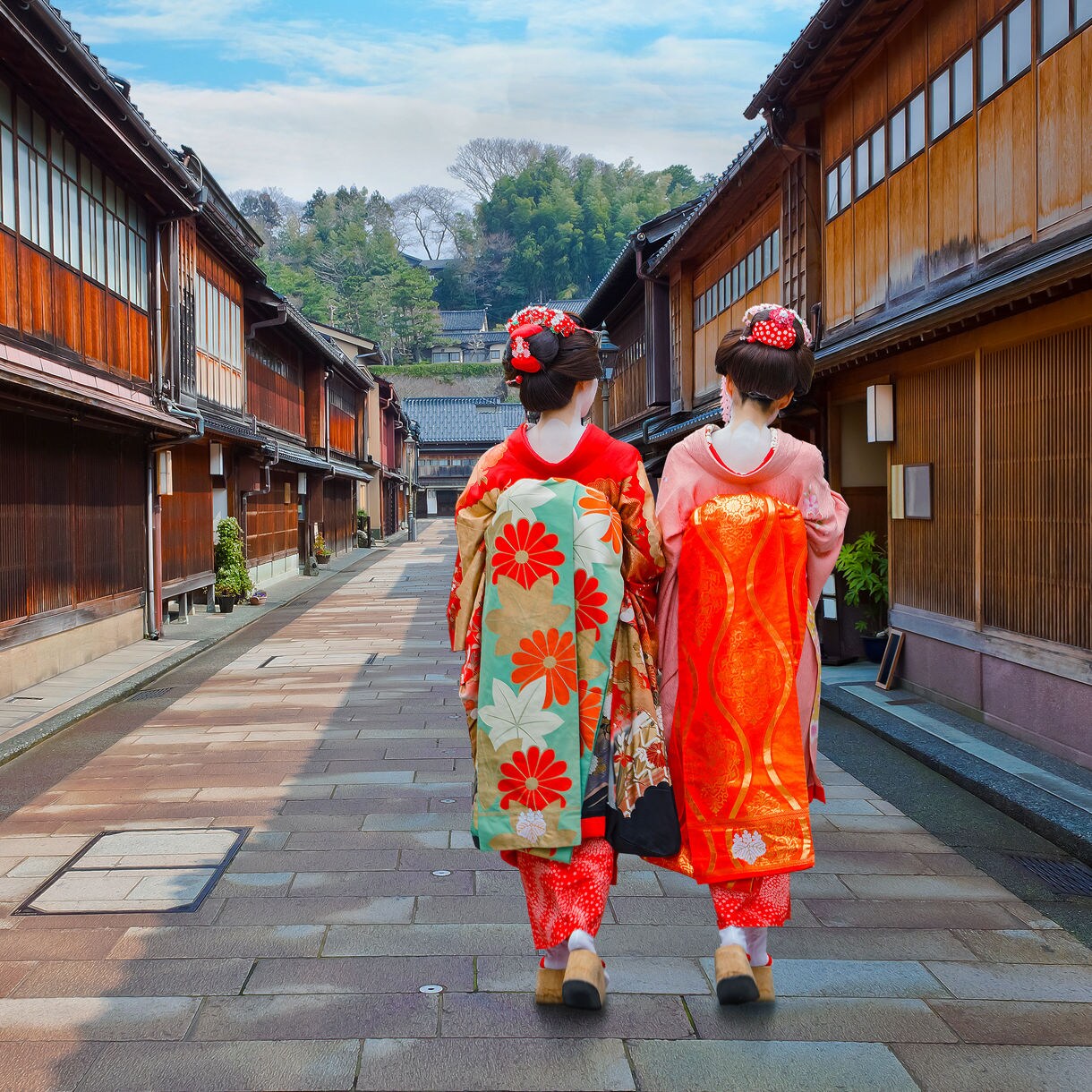 Two women in colorful kimonos walking down a narrow stone street lined with wooden buildings in Kanazawa’s geisha district.