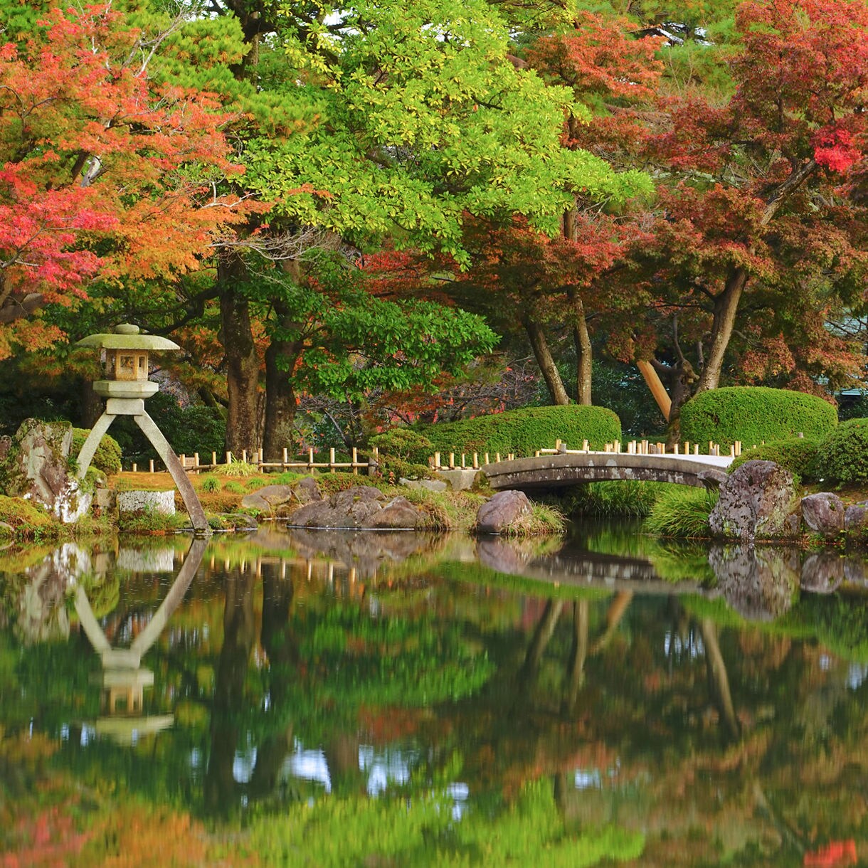 Japanese garden with a stone lantern, arched bridge and colorful autumn trees reflected in a calm pond. Caption: Kanazawa, Japan