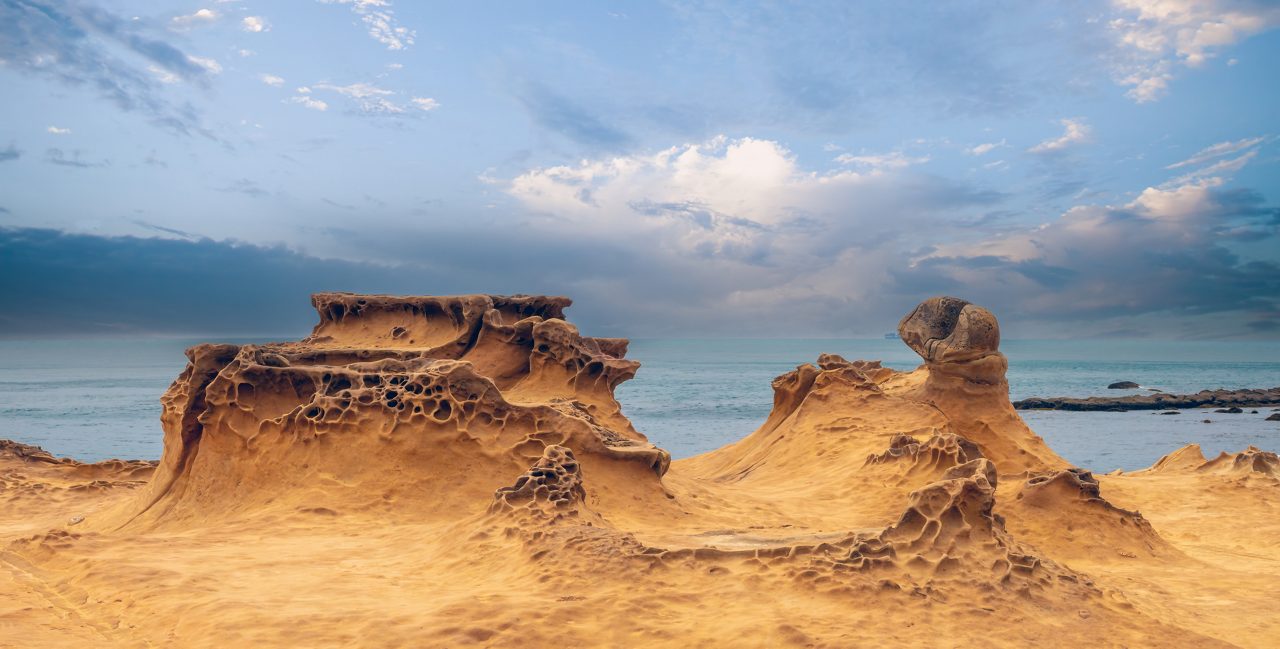 Eroded honeycomb rock formations at Yehliu Geopark in Taiwan with calm sea and partly cloudy sky in the background.